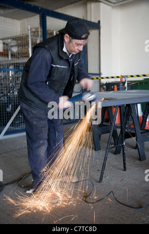 A man grinds a piece of metal after he has finished welding it. Stock Photo