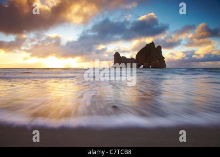 Wharariki Beach. The incoming tides rushes in on Wharariki beach as the sun sets. Looking towards a fascinating large arched roc Stock Photo