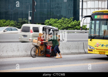 This many is doing it very tough as he pushes his fully laden bicycle across a busy inner city expressway in downtown Guangzhou, China. Stock Photo