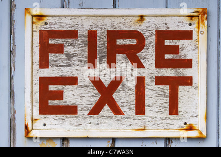 Photo of an old weathered FIRE EXIT sign on a blue door with peeling paint. Stock Photo