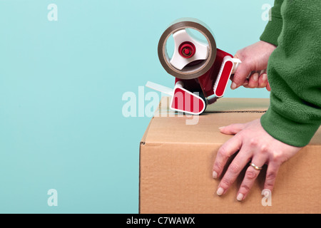 Photo of a womans hands taping up a cardboard box, can be used for removal or logistics related themes. Stock Photo