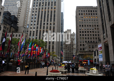 Autumn view, past flower beds and multi-national flags, along Rockefeller Plaza towards 49th Street NBC News Studio, New York Stock Photo