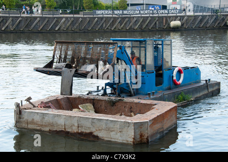 Bucket loader on a barge, clearing floating debris on the Manchester Ship Canal, Salford Quays, Manchester, England, UK Stock Photo