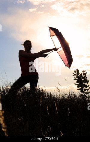 The silhouette of a gymnast stretching with an umbrella in a field ...
