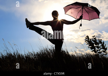The silhouette of a gymnast stretching with an umbrella in a field ...