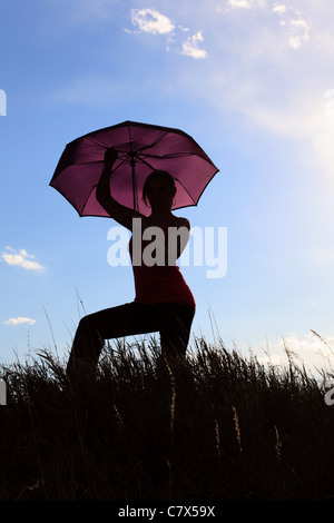 The silhouette of a gymnast stretching with an umbrella in a field ...