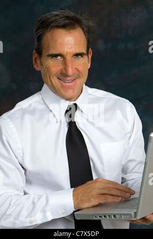 Happy smiling mature businessman, wearing a white shirt and tie, holds a laptop computer and smiles. Stock Photo