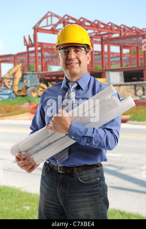 Portrait of engineer at construction site holding plans and wearing a hard hat Stock Photo