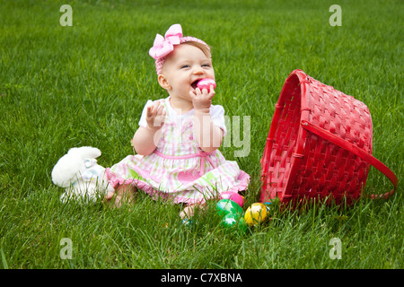 Baby Smiling while holding an Easter egg beside a red basket Stock Photo