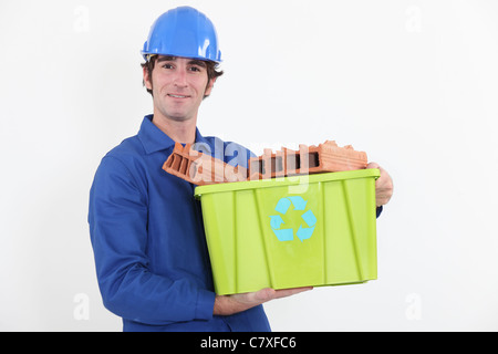 portrait of bricklayer in jumpsuit holding tub full of bricks with recycling logo Stock Photo