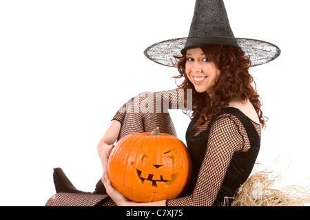 Hispanic teenager girl in black Halloween costume (fishnet dress) sitting on straw with carved pumpkin (jack-o'-lantern) in hand Stock Photo