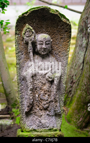 Old weathered stone statue of Jizo, Japanese Buddhist / Shinto guardian of children, in an old garden in Japan. Buddhism; deity; religious statue Stock Photo