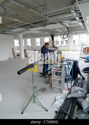 Two men installing cables and tubes in the ceiling of a brand new office building Stock Photo