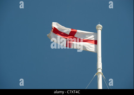 The Cross of St George flag flies from a church flagpole against a blue sky. Stock Photo