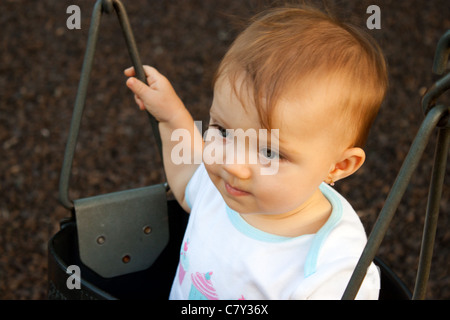 Baby girl staring forward as she swings in a park Stock Photo