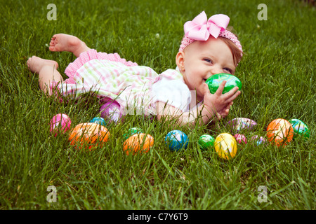 Baby girl laying in the grass with an assortment of colored Easter eggs Stock Photo