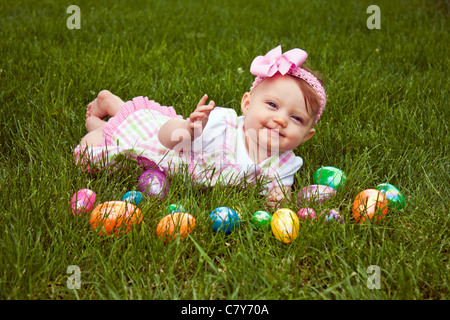 Beautiful baby laying in grass with an assortment of colored Easter eggs Stock Photo