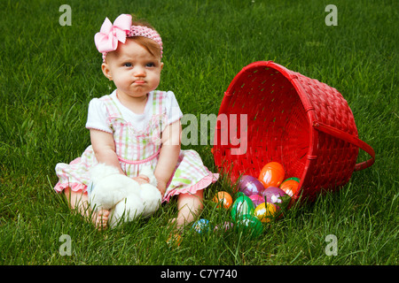 Baby girl frowning beside a spilled Easter egg basket Stock Photo