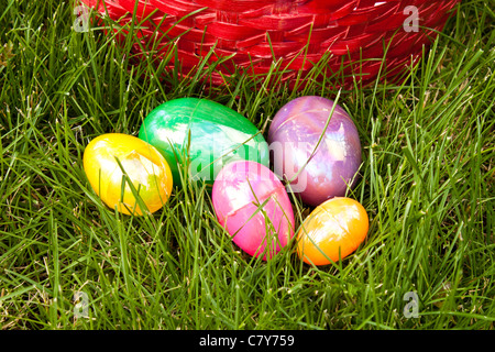 Colored Easter eggs in grass in front of basket Stock Photo