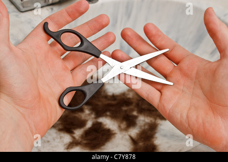 Person regretfully holding scissors with hair in the sink Stock Photo