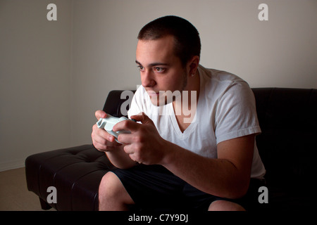 Young man playing a video game in a room lit by the television monitor Stock Photo