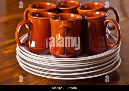 Six ceramic coffee cups sitting on a stack of dinner plates Stock Photo