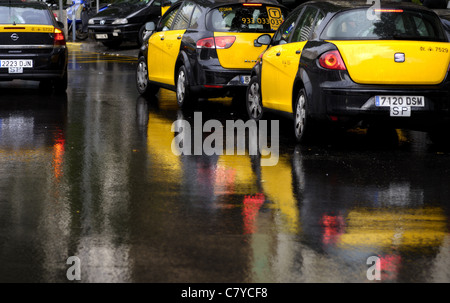 Yellow and black Catalan taxis in Barcelona, Spain with their colour reflected in the wet, rainy road. Stock Photo