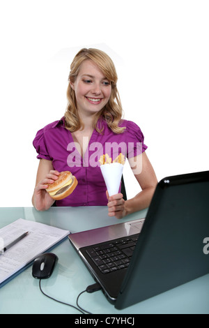 A businesswoman having junk food in her office. Stock Photo