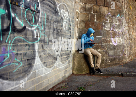 Computer user, hacker, sits conspiratorially with a laptop, in front of a graffiti. Symbol picture, computer-Internet crime. Stock Photo
