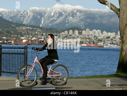 Young Asian woman riding a bicycle along the Stanley Park seawall on a winter day in the City of Vancouver. Stock Photo