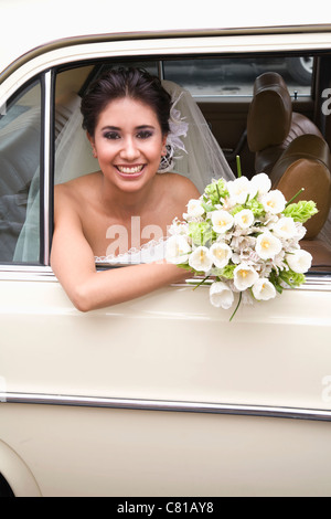 Hispanic bride sitting with bouquet in back of car