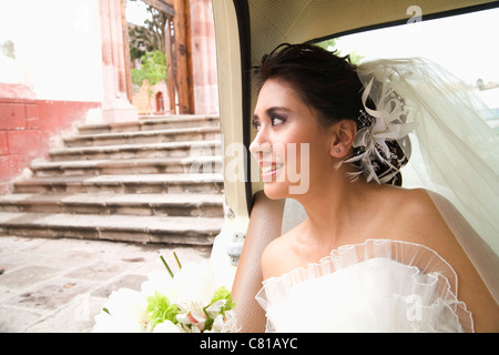 Hispanic bride sitting with bouquet in back of car