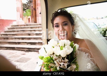 Hispanic bride sitting with bouquet in back of car