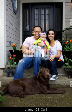 Mother and father sitting on front stoop with baby girl and dog Stock Photo