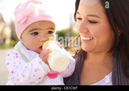 Mixed race mother watching baby girl drinking bottle Stock Photo