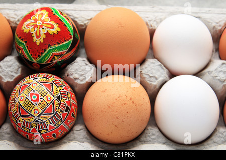 6 eggs in a carton including 2 white, 2 brown, and 2 red pysanka Easter eggs Stock Photo