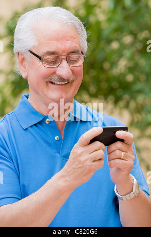 Senior Hispanic man text messaging on cell phone Stock Photo