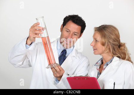 Man and woman in white coats with clipboard, examining orange liquid Stock Photo