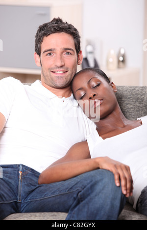 young couple, white man watching us and black woman sleeping on him Stock Photo