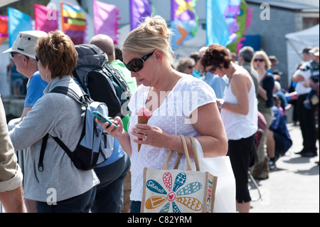 Cornwall, UK - Woman eating ice cream while using mobile phone Stock Photo