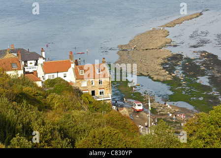 Exposed rocks at low-tide at Robin Hoods bay in Yorkshire and a mobile ice-cream van on the beach. Stock Photo