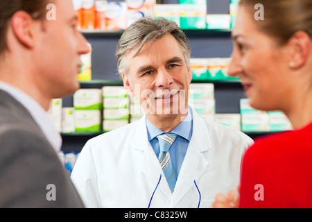 Pharmacist is consulting customers - a man and a woman - in his pharmacy Stock Photo