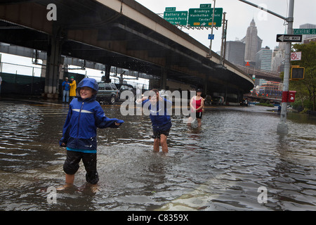 Flooded street under Manhattan Bridge in NYC, during Hurricane Irene. Kids playing with water. New York City, USA Stock Photo