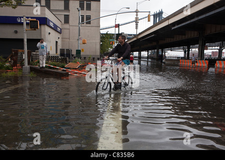 Biker on flooded street under Manhattan Bridge, NYC, during hurricane Irene. New York City, USA Stock Photo