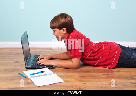 Photo of a boy lying on the floor typing on his laptop computer Stock Photo