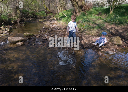 Little Boy and Baby Girl Playing Throwing Pebbles into the River, Hathersage, Peak District, Derbyshire, UK Stock Photo