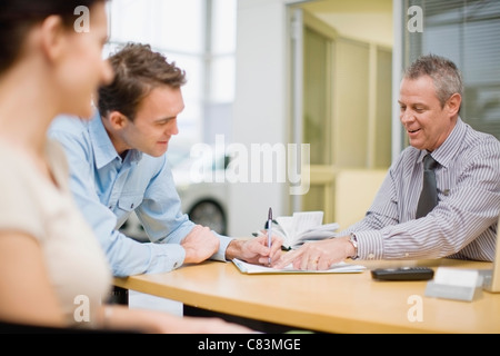 Couple signing papers with car salesman Stock Photo