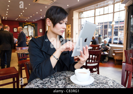 Young woman browsing the Internet on an Apple iPad tablet computer using free coffee shop wi fi, London, UK Stock Photo