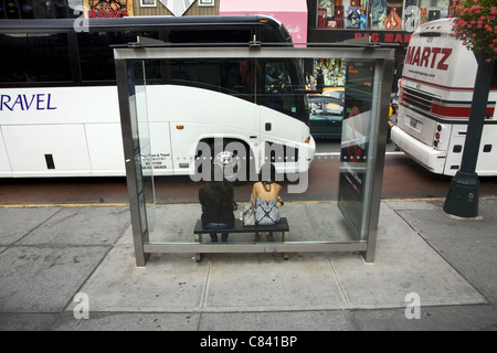 Two women wait for a city bus on 34th Street in NYC Stock Photo