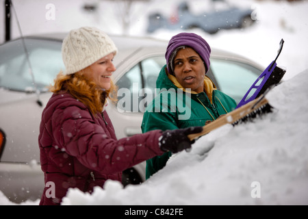 Two women scraping snow from windshield Stock Photo